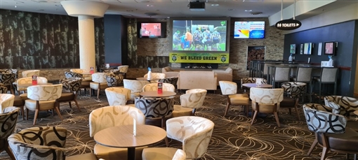The Sports Bar: armchairs around tables, and big screens under a We Bleed Green banner